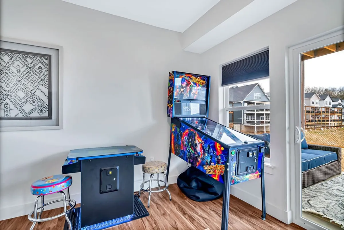 This image captures a vibrant game room setup with a pinball machine and arcade game, surrounded by bar stools. The atmosphere is lively, inviting guests to play, compete, and enjoy moments of nostalgia. The fun and social environment is highlighted by the energetic lighting and arrangement.