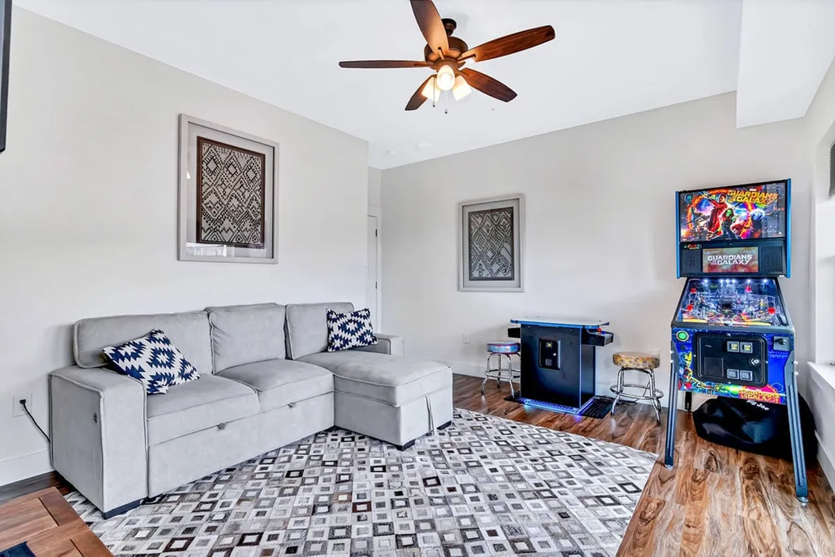 This lively game room is furnished with a sectional sofa, arcade machine, and game table, all set in a casual and fun environment. The space is designed for playful gatherings, celebrations, and quiet relaxation.