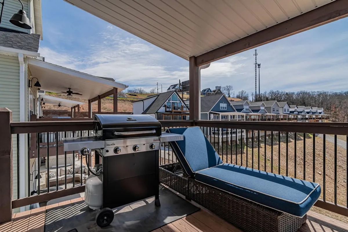 A cozy balcony setup featuring a grill and lounge chair, positioned to take in views over the landscape. The scene suggests the enjoyment of grilling meals outdoors, relaxing in the fresh air, and watching the sun set beyond the railing.