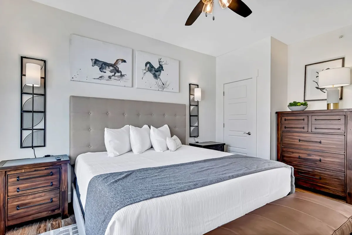 A tranquil bedroom featuring a bed with decorative pillows, horse-themed artwork, nightstands with lamps, and a dresser. Soft lighting and a welcoming color palette create an inviting, restful atmosphere.