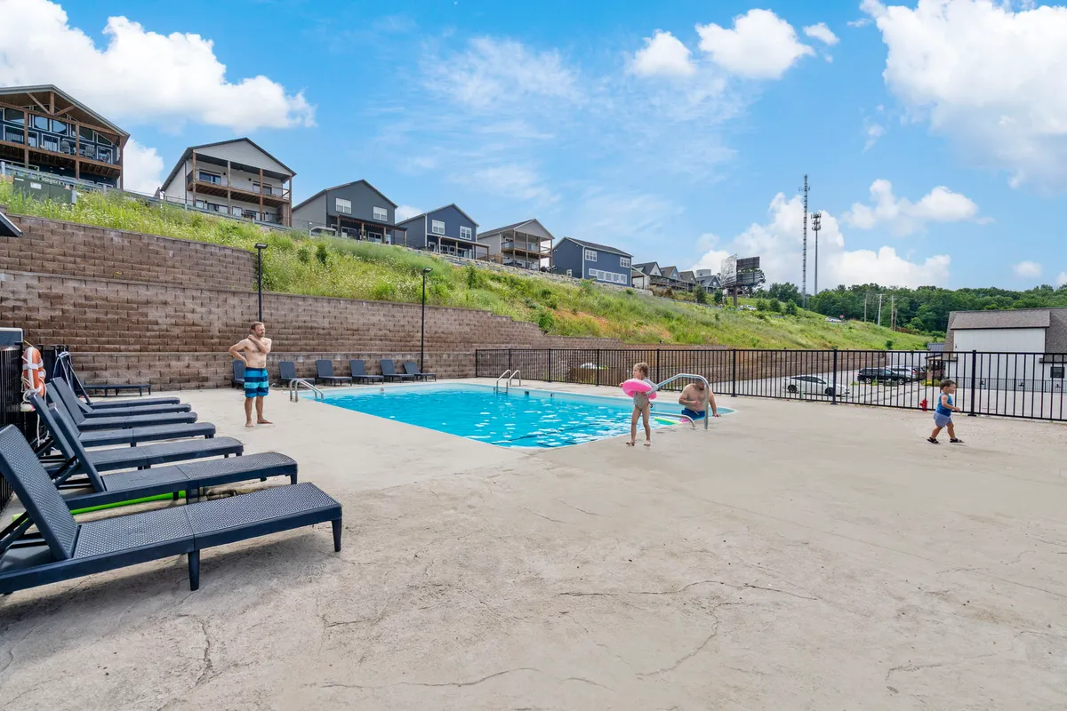 A vibrant swimming pool scene with families and children playing, adults relaxing on lounge chairs, and the pool beautifully reflecting the colors of sunset. The area is lively and joyful, emphasizing summer fun and resort amenities.