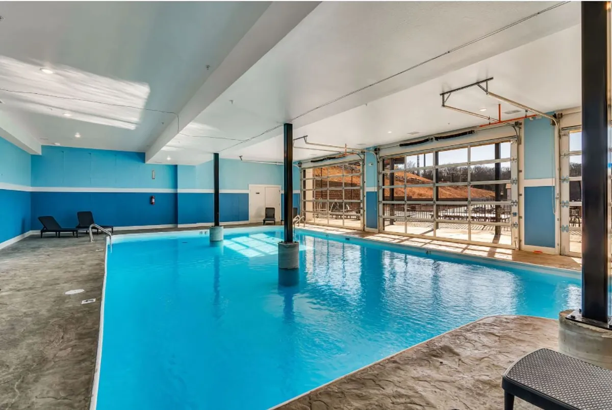 A refreshing indoor swimming pool is surrounded by a wooden deck and large windows, allowing in abundant natural light. The space is serene and welcoming, ideal for year-round swimming and quiet relaxation regardless of the weather.