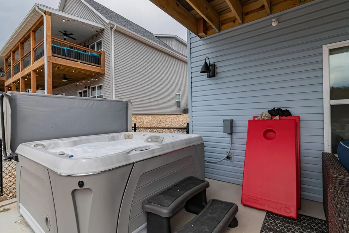 An inviting outdoor setting with a private hot tub, steps leading down to it, and the house exterior as a backdrop. The area feels cozy and secluded, ideal for a soothing soak or relaxed gathering after a day of games.