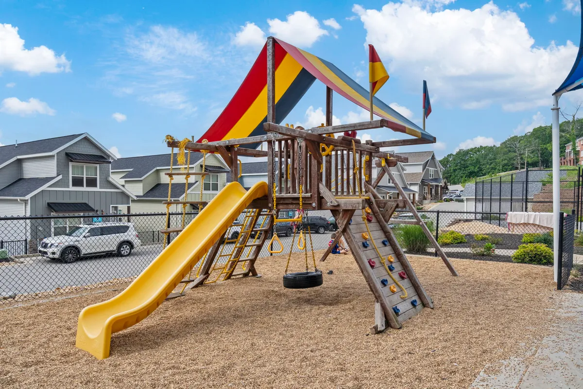 A colorful playground structure with slide, swing set, and climbing wall, bustling with children playing and families gathering nearby. The mood is cheerful and energetic, emphasizing safe and joyful family fun.