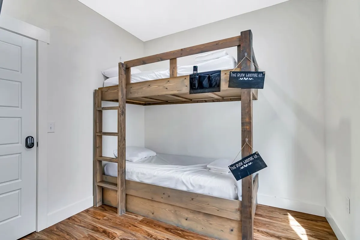 A playful bunk room featuring a sturdy bunk bed with wooden textures and cozy white bedding. The layout encourages both rest and play, making it perfect for kids to create their own adventures or unwind after arcade fun. The room exudes a relaxed and welcoming vibe.
